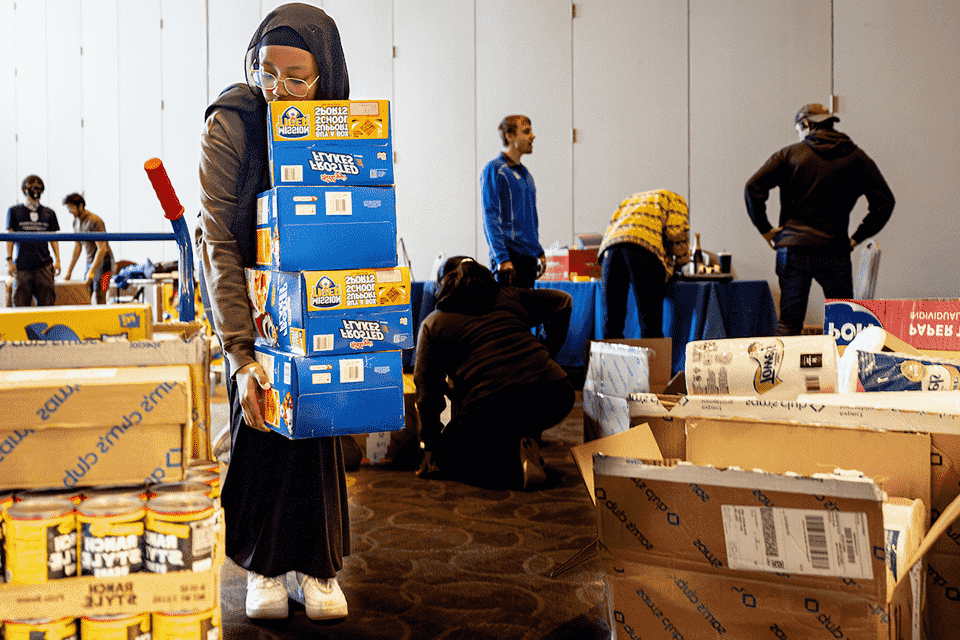 A student carries several large boxes of Frosted Flakes cereal while others work around her.