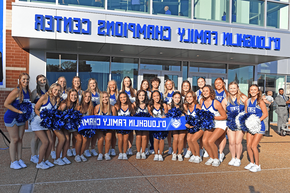 A group of cheerleaders pose for a photo with a banner that states o'loughlin family champions center