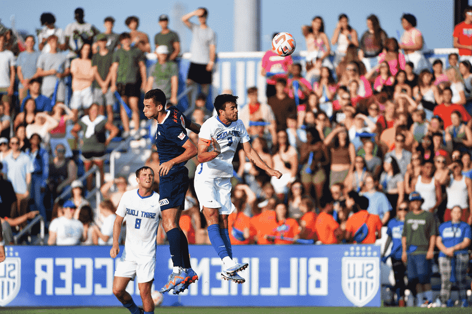 Men's soccer player headbutts the ball away from an opponent.